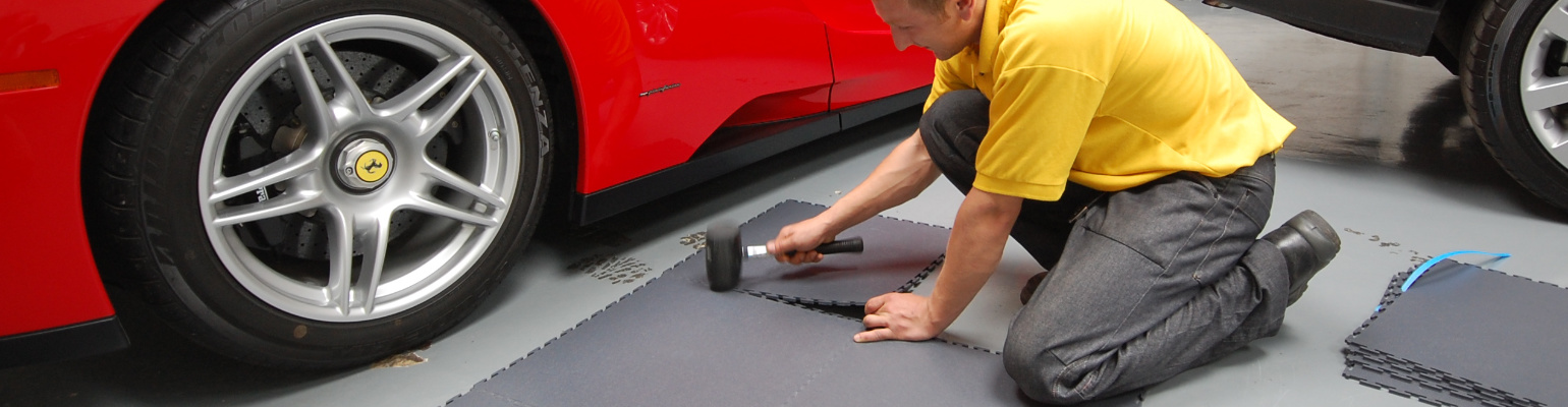 Garage flooring PVC tiles being laid using a rubber mallet next to a Ferrari.
